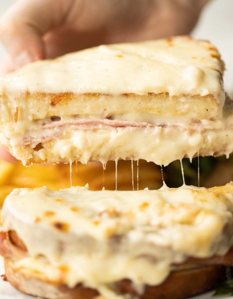 close up shot of hand lifting half of croque monsieur showing filling