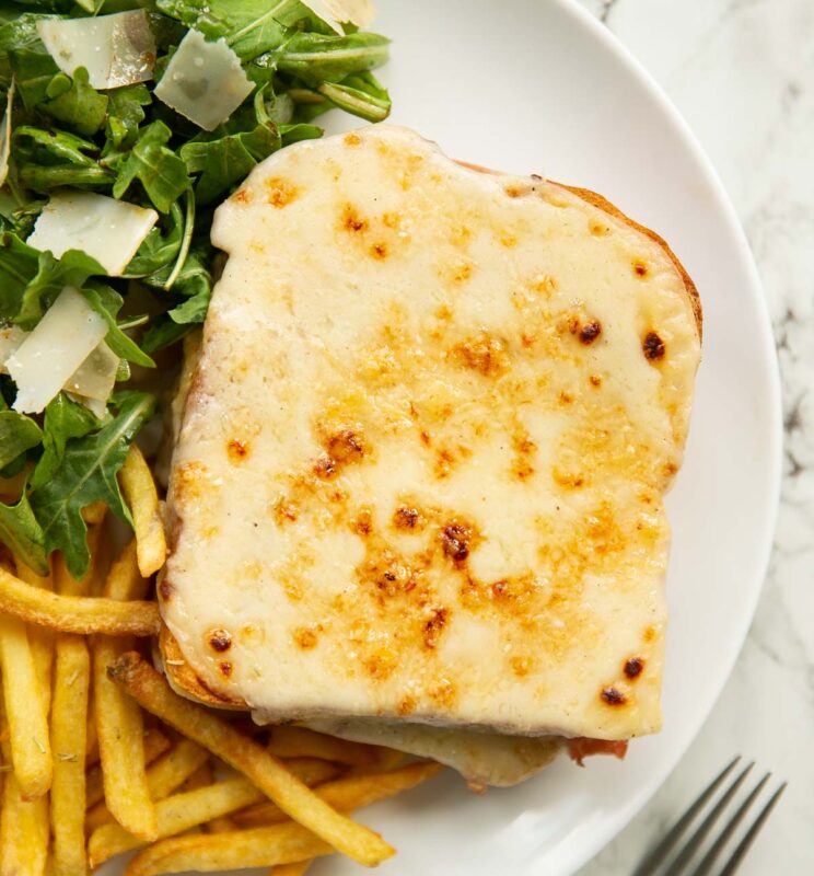 overhead shot of croque monsieur on large white plate with fries and salad