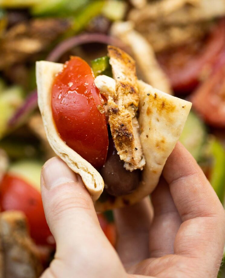 close up overhead shot of hand holding folded flatbread with greek chicken salad