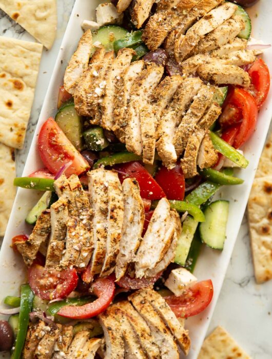overhead shot of greek chicken salad served on large rectangular white dish surround by flatbread