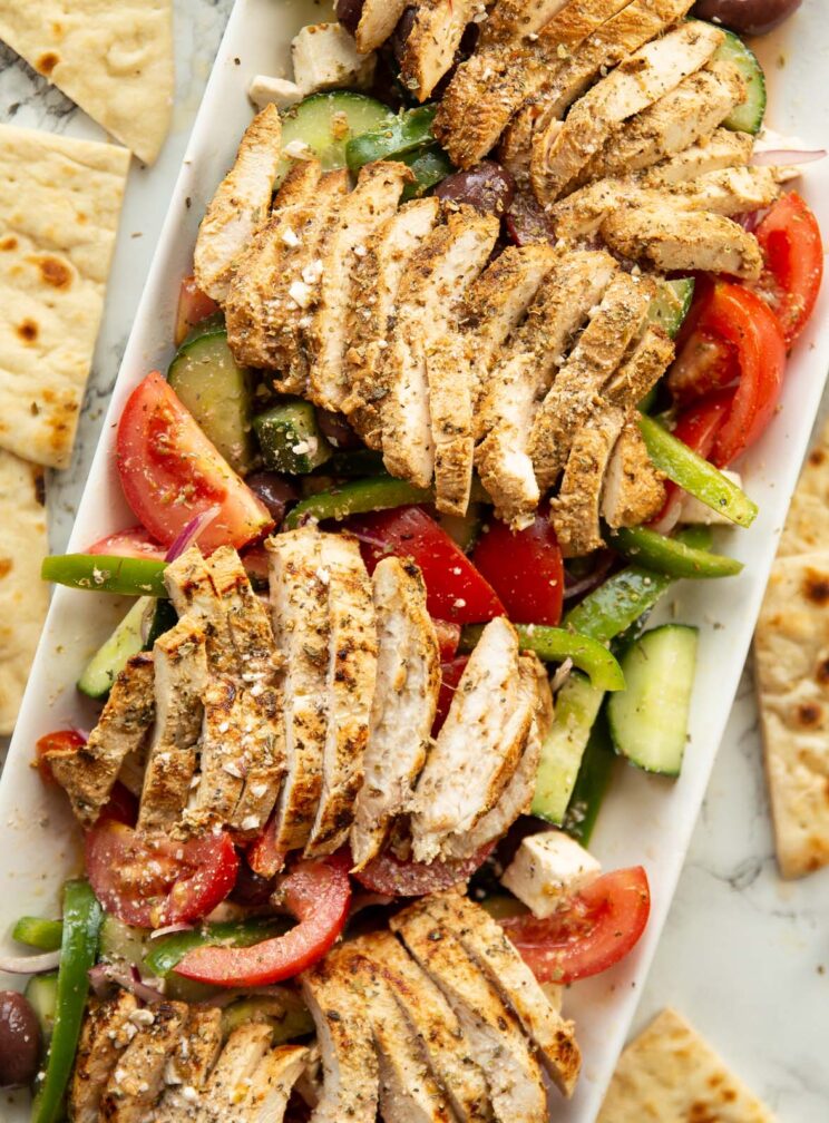 overhead shot of greek chicken salad served on large rectangular white dish surround by flatbread