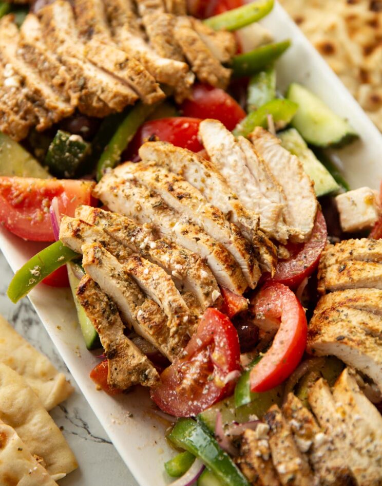 close up shot of sliced chicken on greek salad