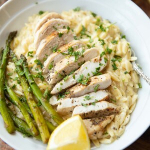 close up shot of lemon chicken orzo served in white bowl garnished with fresh parsley