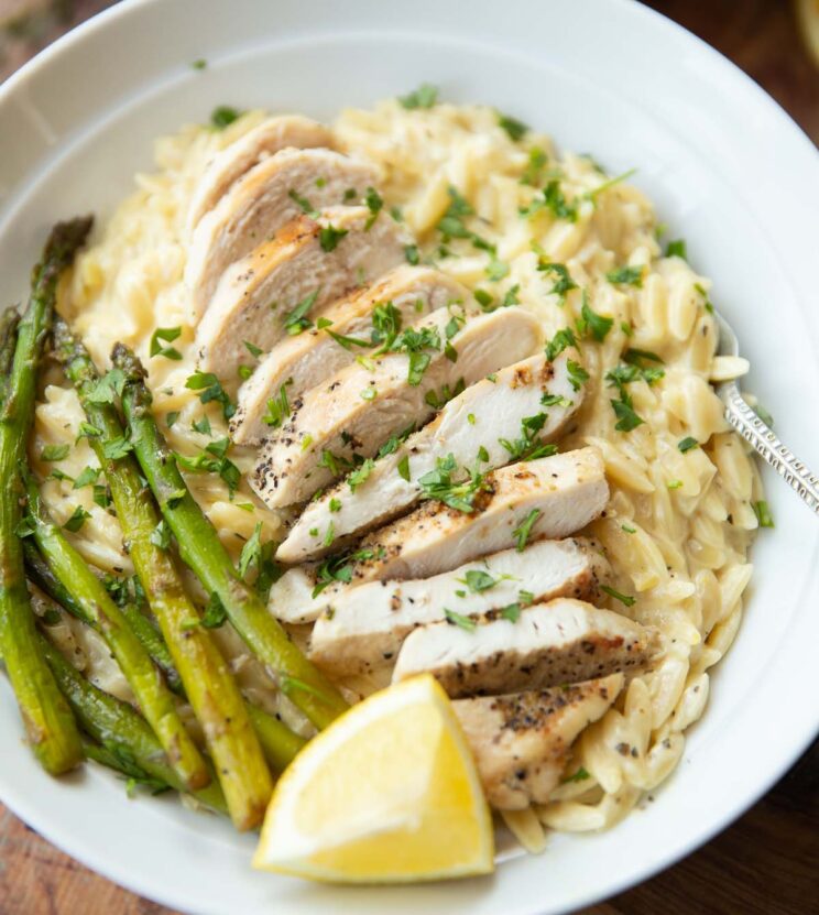 close up shot of lemon chicken orzo served in white bowl garnished with fresh parsley