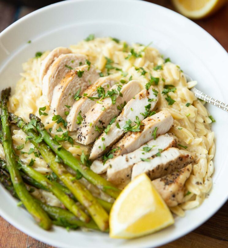 close up shot of lemon chicken orzo in white bowl with fresh parsley