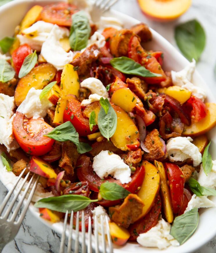 close up shot of peach tomato salad in large white dish garnished with fresh basil