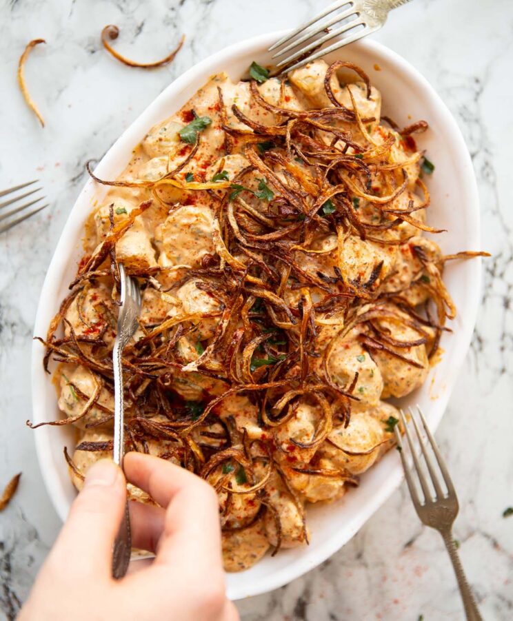 overhead shot of spicy cajun potato salad in large white dish with hand digging in with silver fork