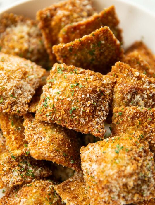 close up shot of toasted ravioli in large white dish