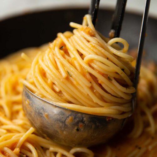 close up shot of tomato butter pasta in silver ladle