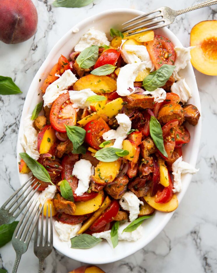 overhead shot of tomato peach salad in large white dish garnished with fresh basil