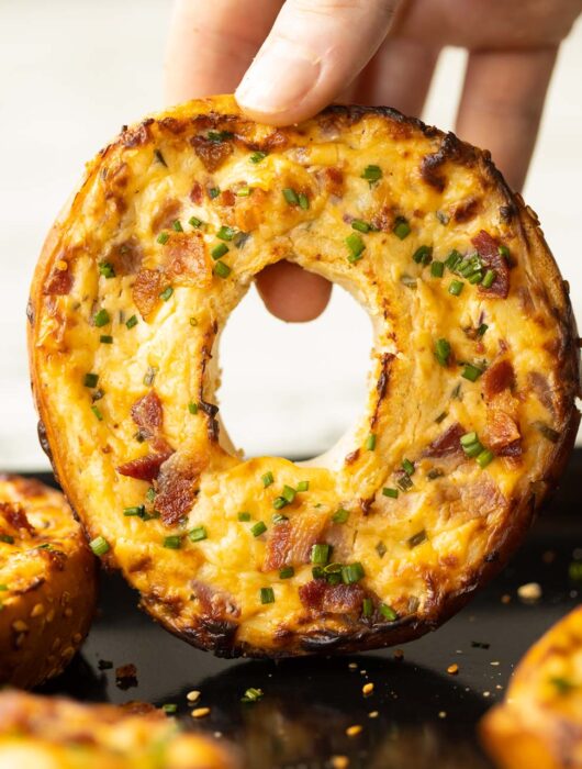 close up shot of hand holding bagel above baking tray