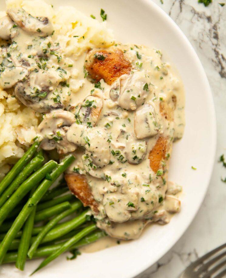 overhead shot of creamy garlic and mushroom chicken served on white plate with green beans and mash