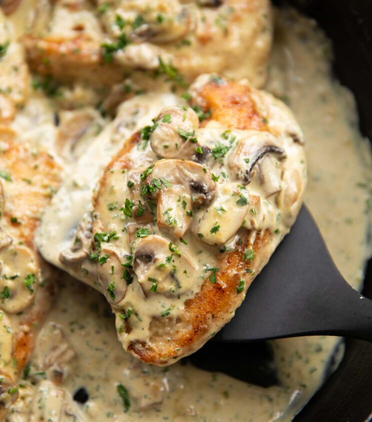 close up shot of black spatula lifting creamy garlic mushroom chicken out of cast iron skillet