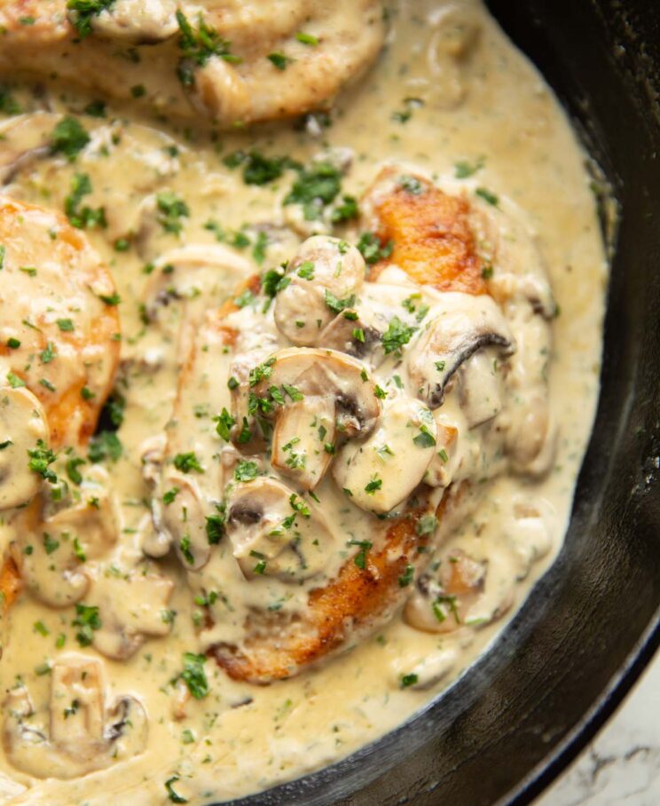 close up shot of creamy mushroom garlic chicken in cast iron skillet garnished with parsley