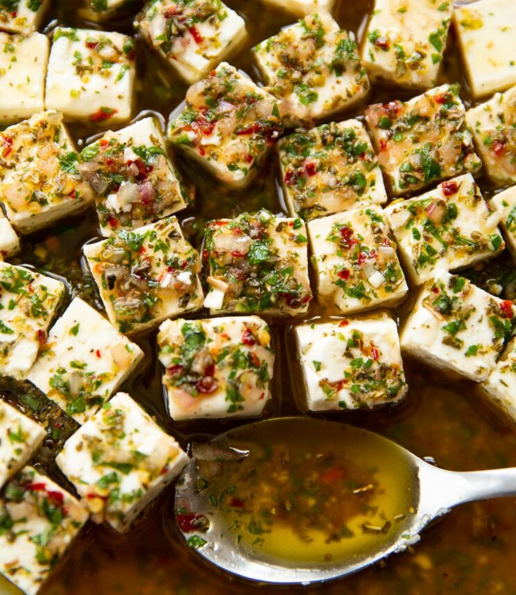 close up shot of marinated feta in glass dish with silver spoon