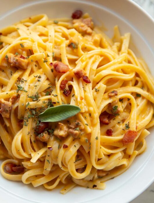 close up shot of roasted butternut squash pasta in white bowl garnished with fresh sage