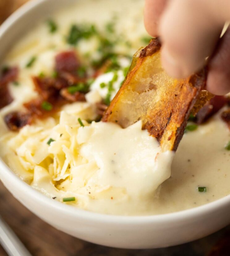 hand dunking potato skin into small white bowl of baked potato soup