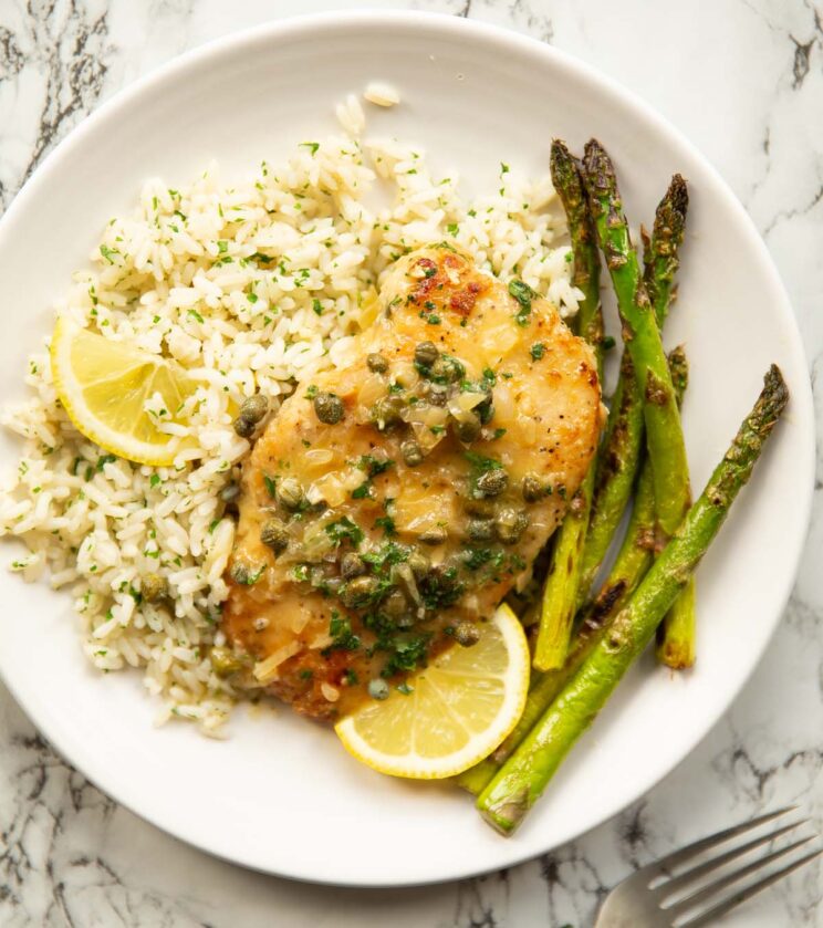overhead shot of chicken piccata served on small whit eplate with asparagus and rice