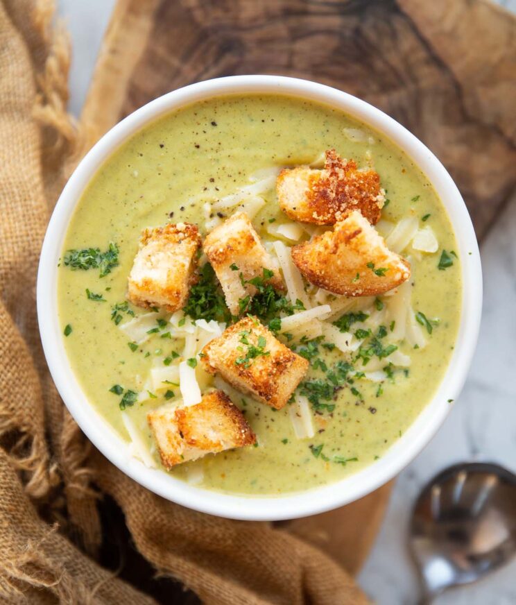 overhead shot of broccoli cheddar soup in small white bowl on wooden chopping board