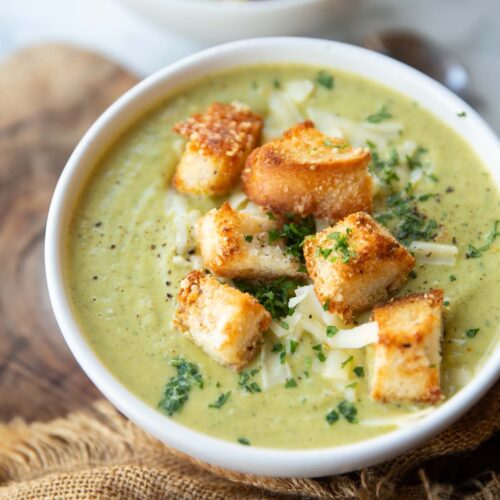 close up side shot of broccoli soup in small white bowl with cheesy croutons