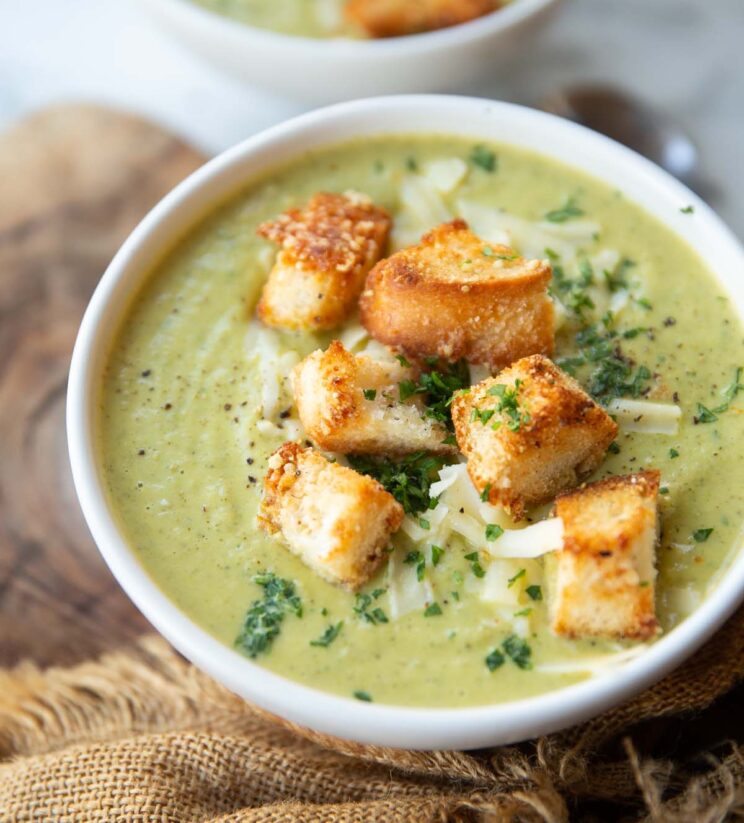 close up side shot of broccoli soup in small white bowl with cheesy croutons