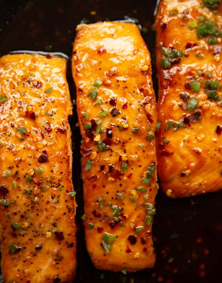 overhead shot of 3 salmon fillet sin pan garnished with chilli flakes and spring onion