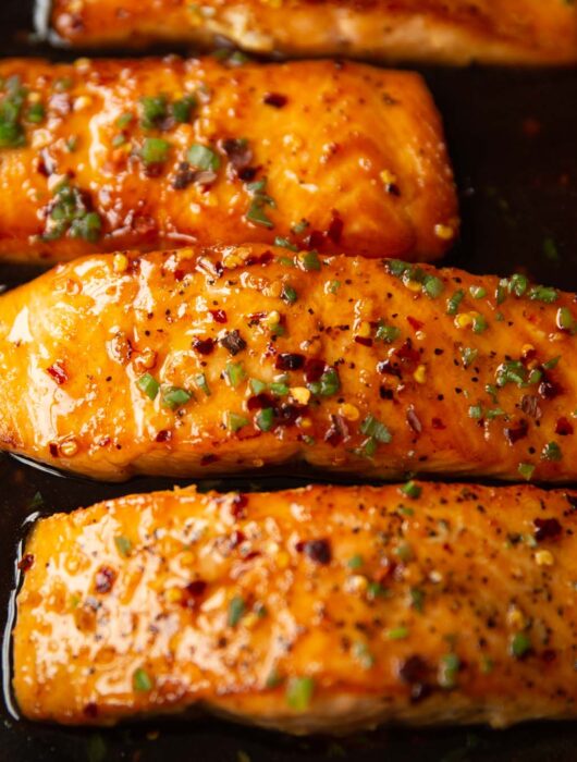 4 salmon fillets in pan garnished with spring onion and chilli flakes