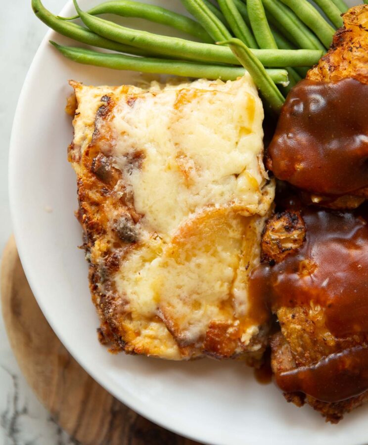 overhead shot of portion of leek and potato gratin on plate with chicken thighs and green beans