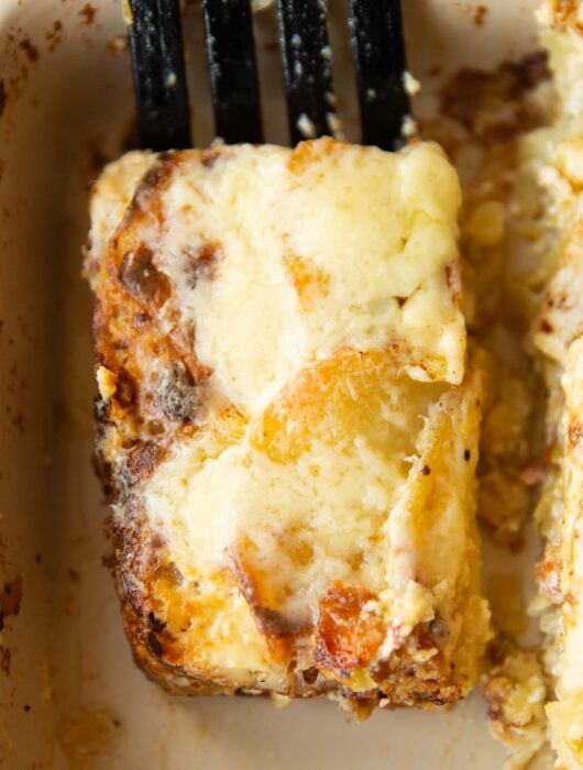 close up overhead shot of black spatula lifting portion of leek bacon potato gratin