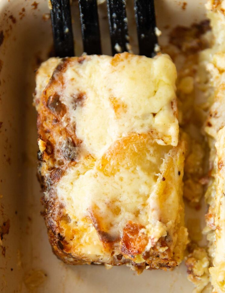 close up overhead shot of black spatula lifting portion of leek bacon potato gratin