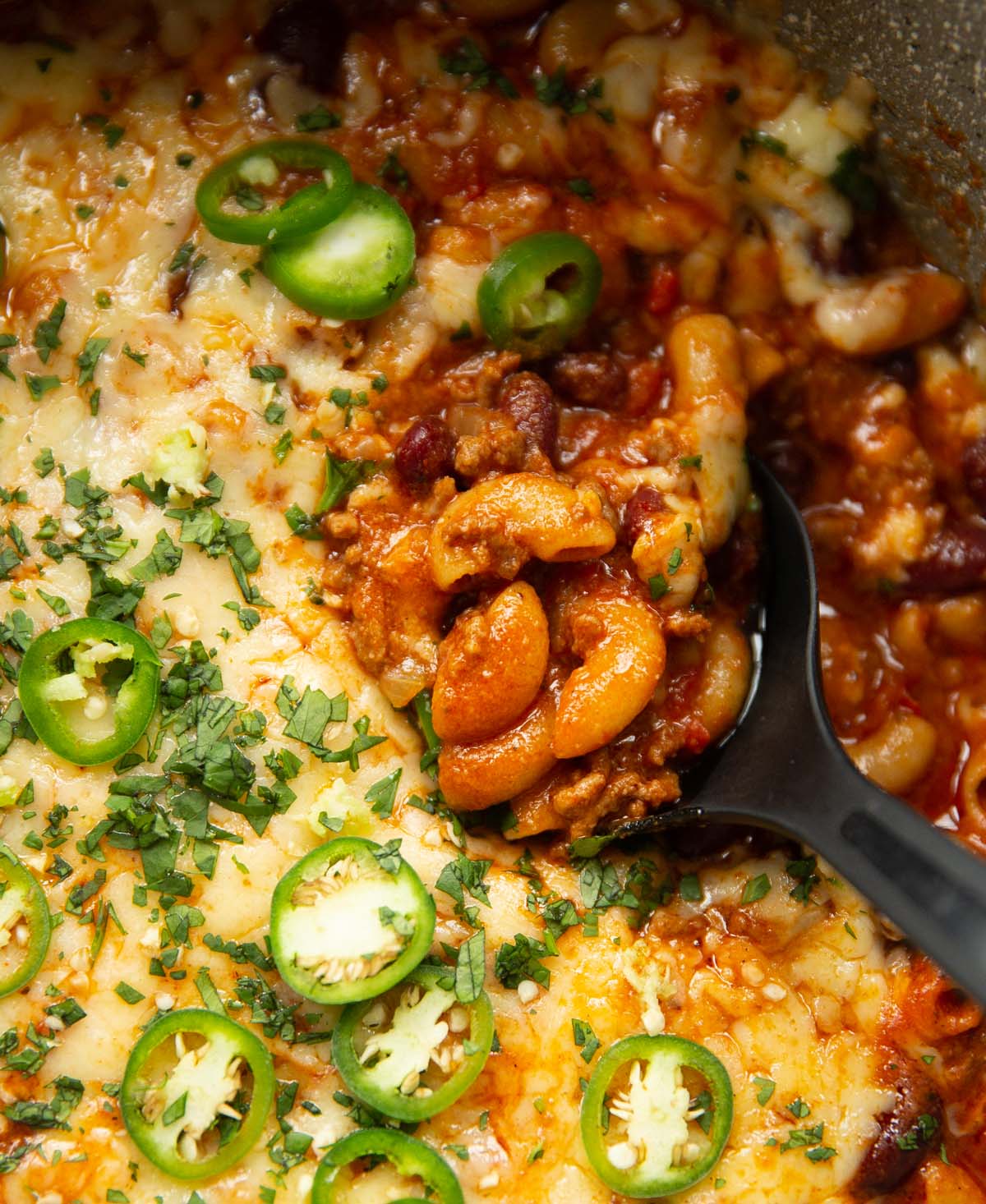 overhead close up shot of black serving spoon digging into pot of chili mac