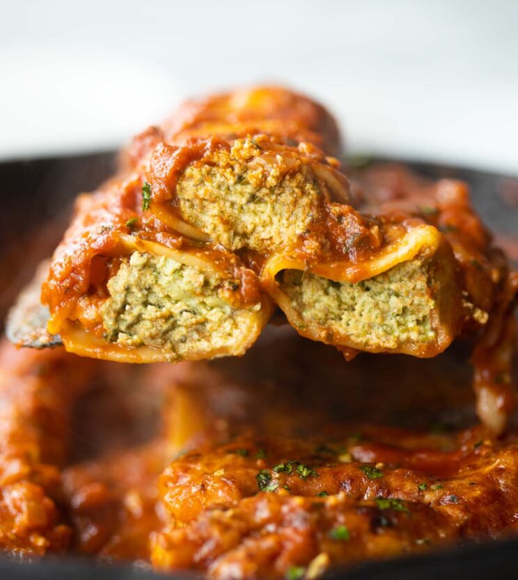 close up shot of black spatula lifting 3 pesto ricotta cannelloni out of cast iron skillet