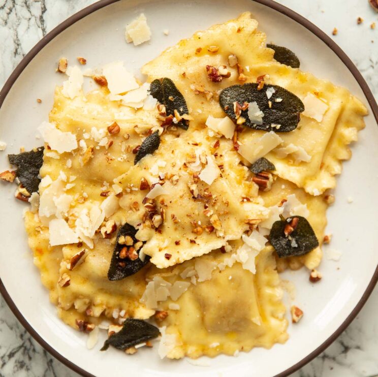 overhead shot of ravioli served on small white plate on marble backdrop