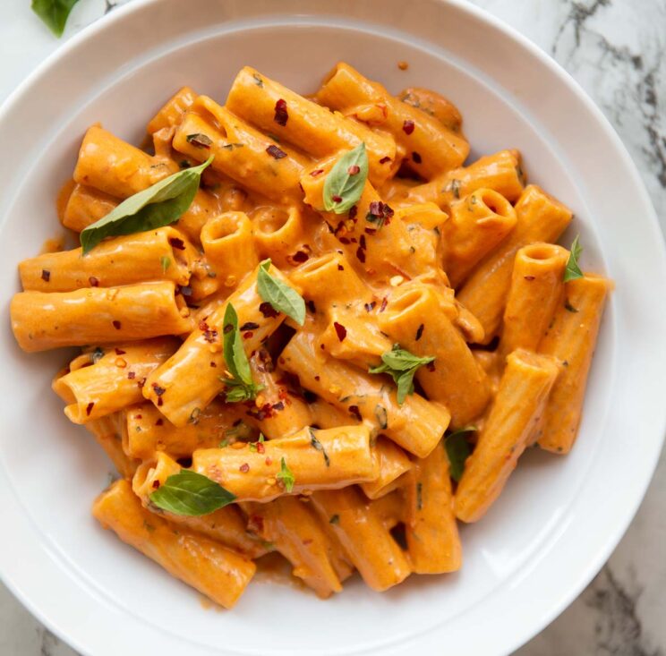 overhead shot of spicy rigatoni in large white bowl garnished with fresh basil