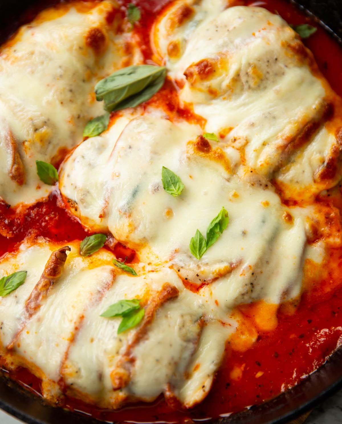 close up shot of hasselback chicken in skillet fresh out the oven garnished with fresh basil