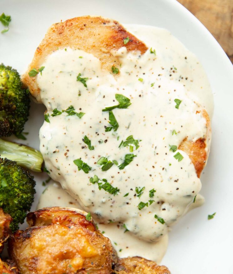 close up overhead shot of chicken breast and creamy garlic sauce on white plate with broccoli and smashed potatoes