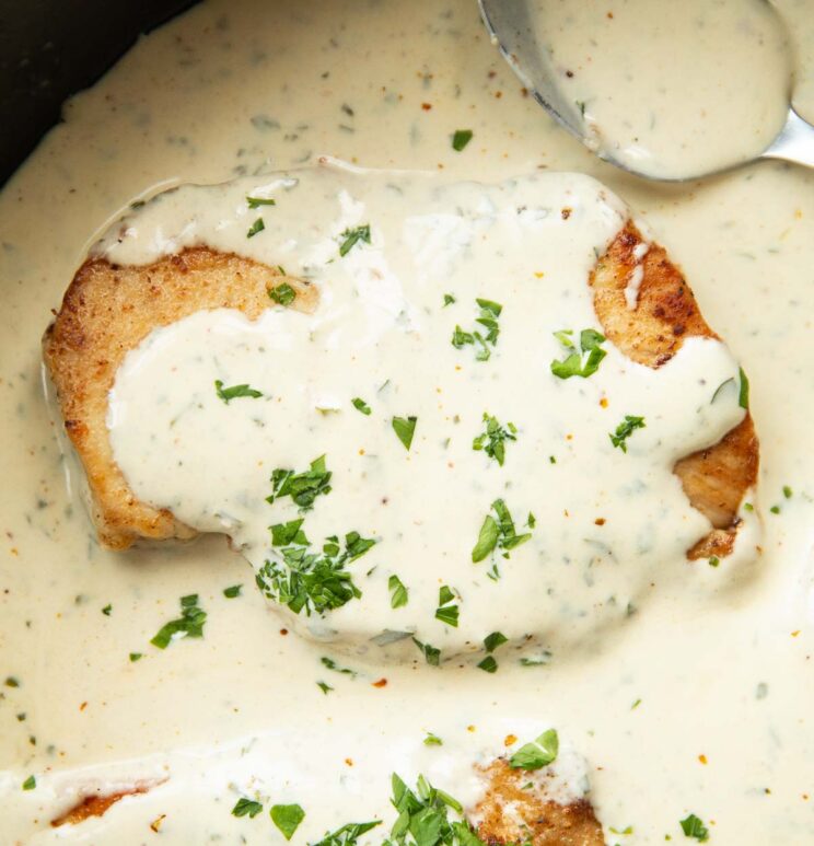 close up shot of creamy garlic chicken in large cast iron skillet with spoon in background