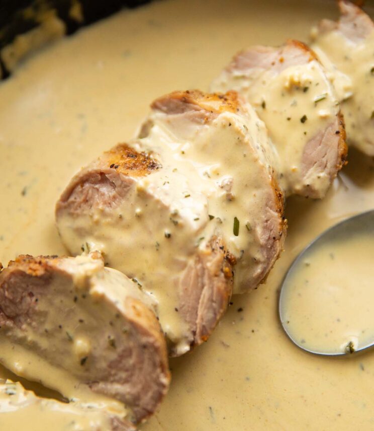 close up shot of sliced pork tenderloin in skillet of creamy mustard sauce