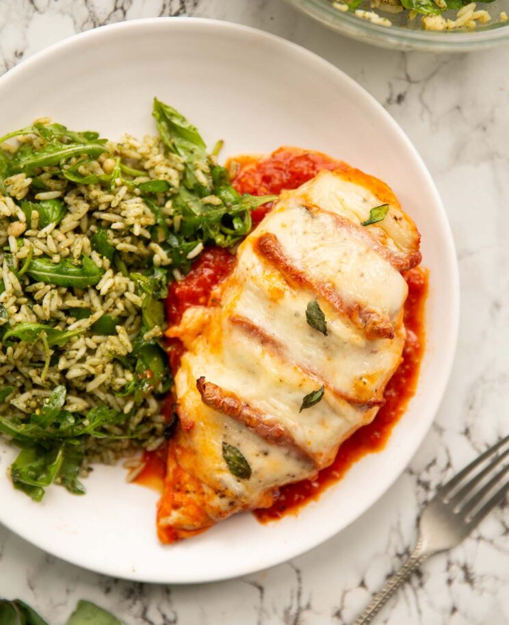 overhead shot of hasselback chicken served with pesto rice on small white plate