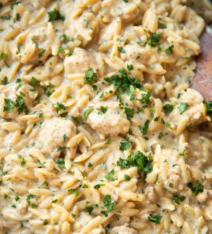 close up shot of parmesan garlic sausage orzo in skillet with wooden spoon digging in