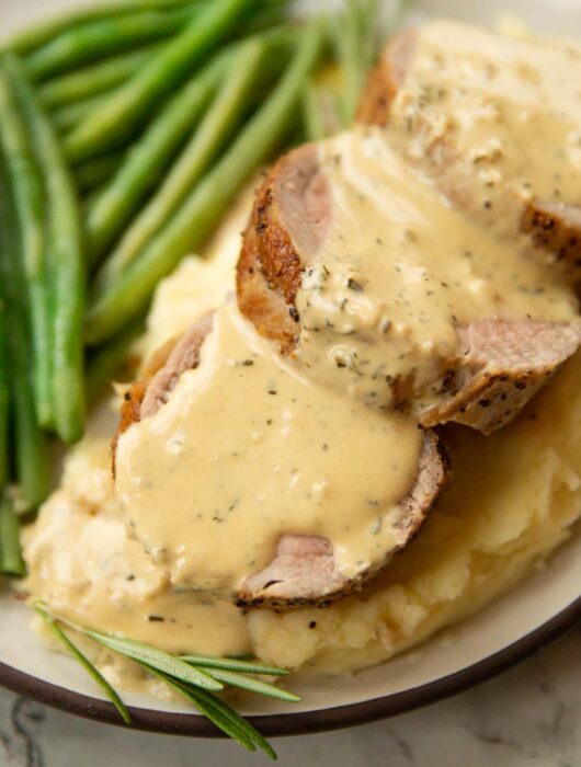 close up shot of pork tenderloin slices on mashed potato with mustard sauce and green beans blurred in background