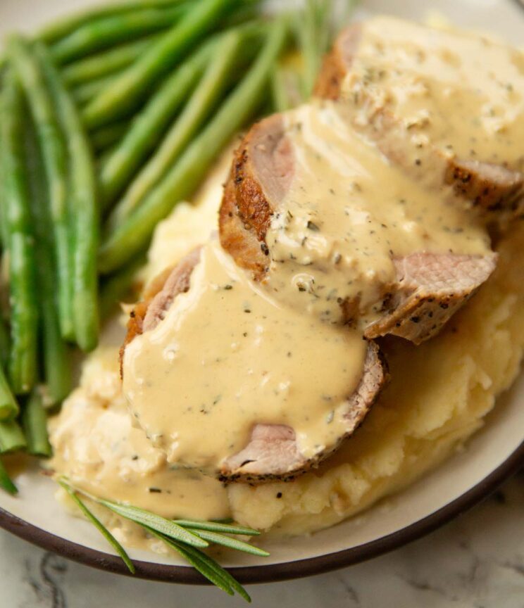 close up shot of pork tenderloin slices on mashed potato with mustard sauce and green beans blurred in background