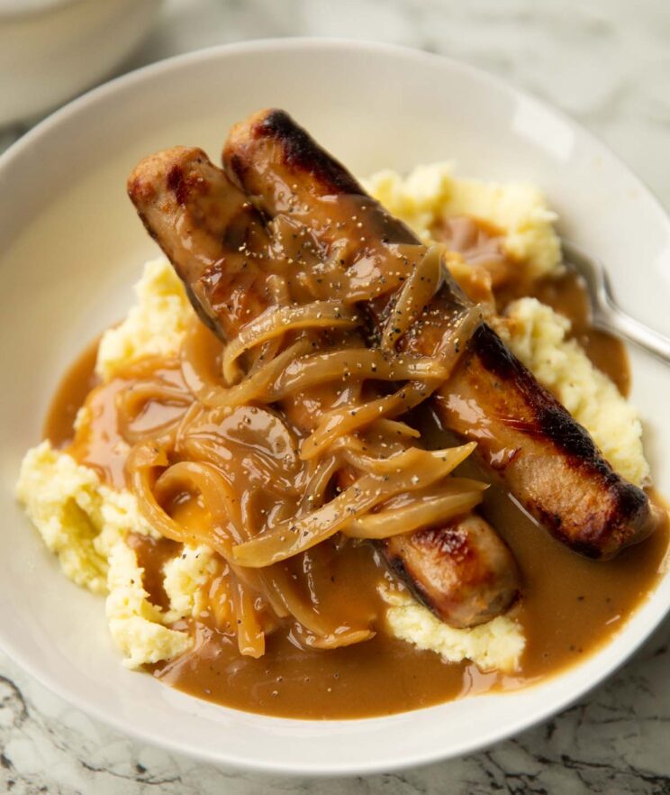 side shot of bangers and mash with onion gravy in large white bowl