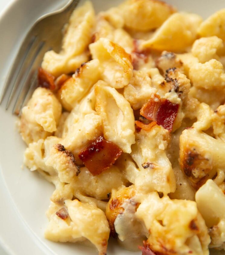 close up shot of cheesy cauliflower pasta in white bowl with silver fork blurred in background