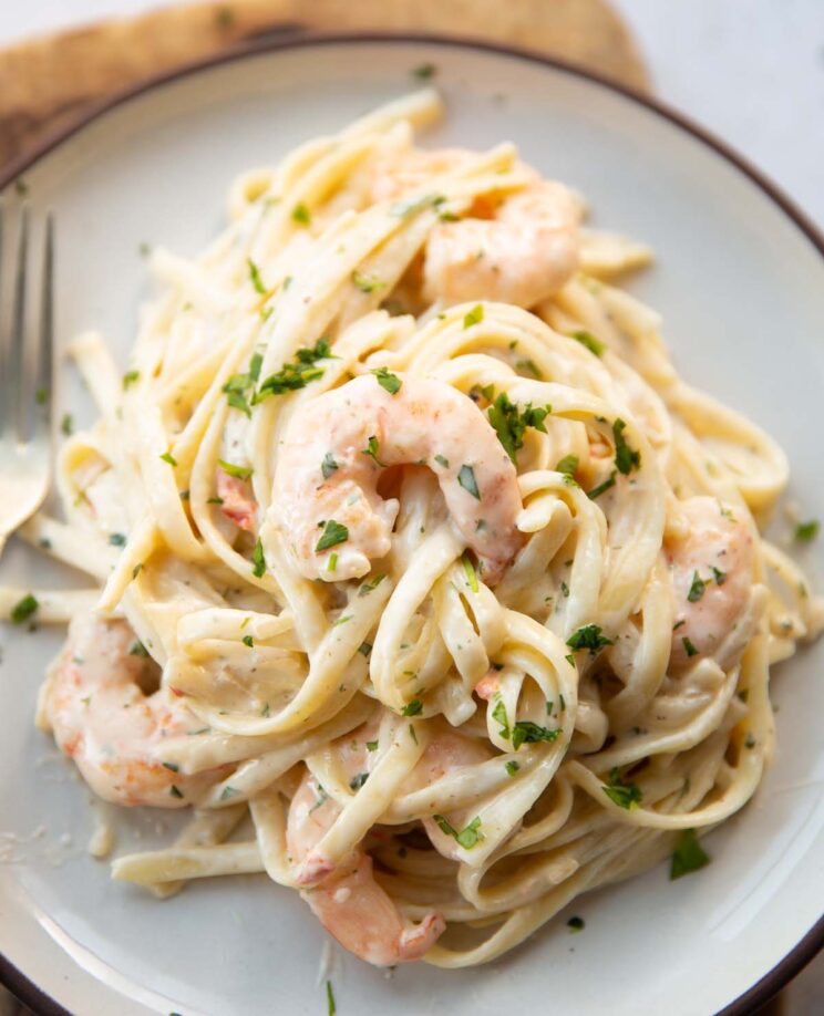 close up shot of creamy prawn linguine on small white plate with silver fork on the side