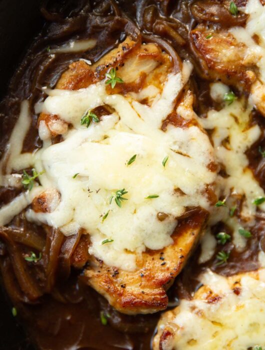 close up shot of french onion pork chop in skillet garnished with fresh thyme