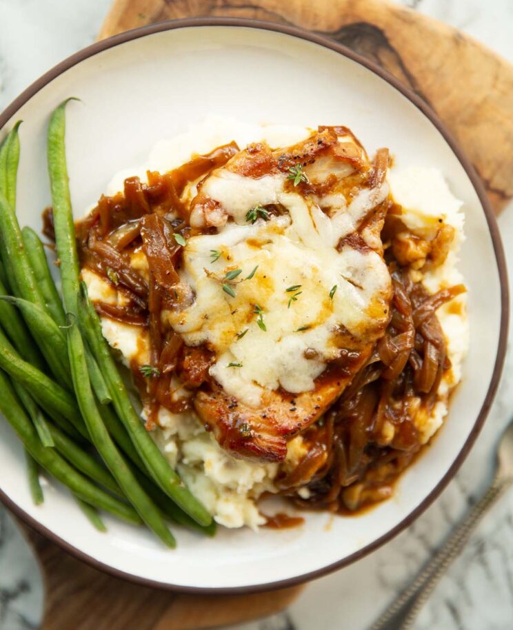 overhead shot of french onion pork chop served on bed of mashed potato with green beans on small white plate