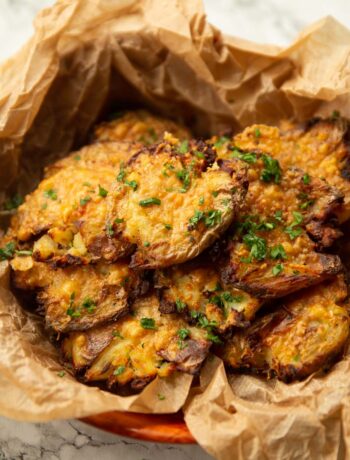 close up shot of parmesan smashed potatoes in scrunched up parchment paper garnished with parsley