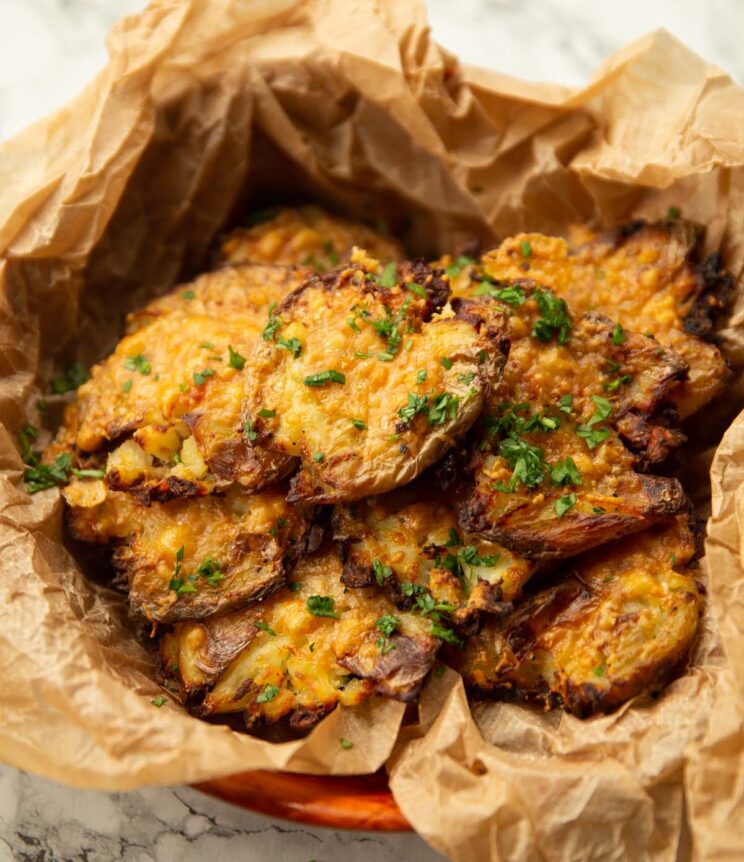 close up shot of parmesan smashed potatoes in scrunched up parchment paper garnished with parsley