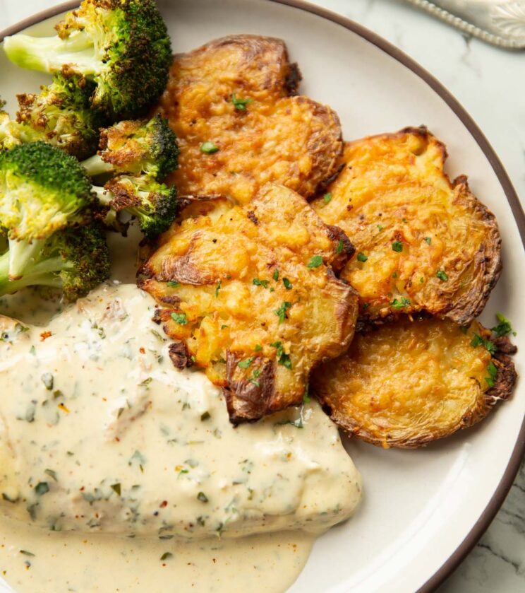 close up shot of smashed potatoes on small white plate with chicken and broccoli